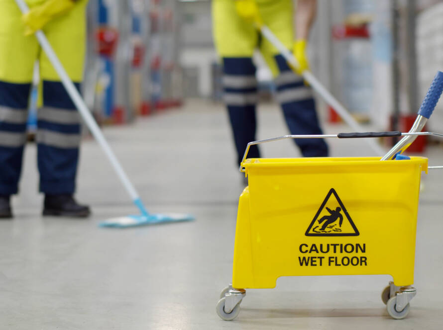 Cropped shot of worker swearing safety overall holding mop cleaning floor in warehouse. Team of janitors with bucket washing floor in industrial storehouse